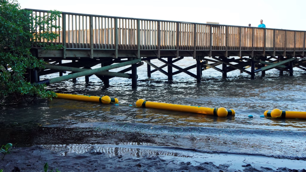 Retenedores flotantes instalados en la ciénaga de Mallorquín, con un muelle de madera y dos personas observando el ecosistema desde la pasarela.