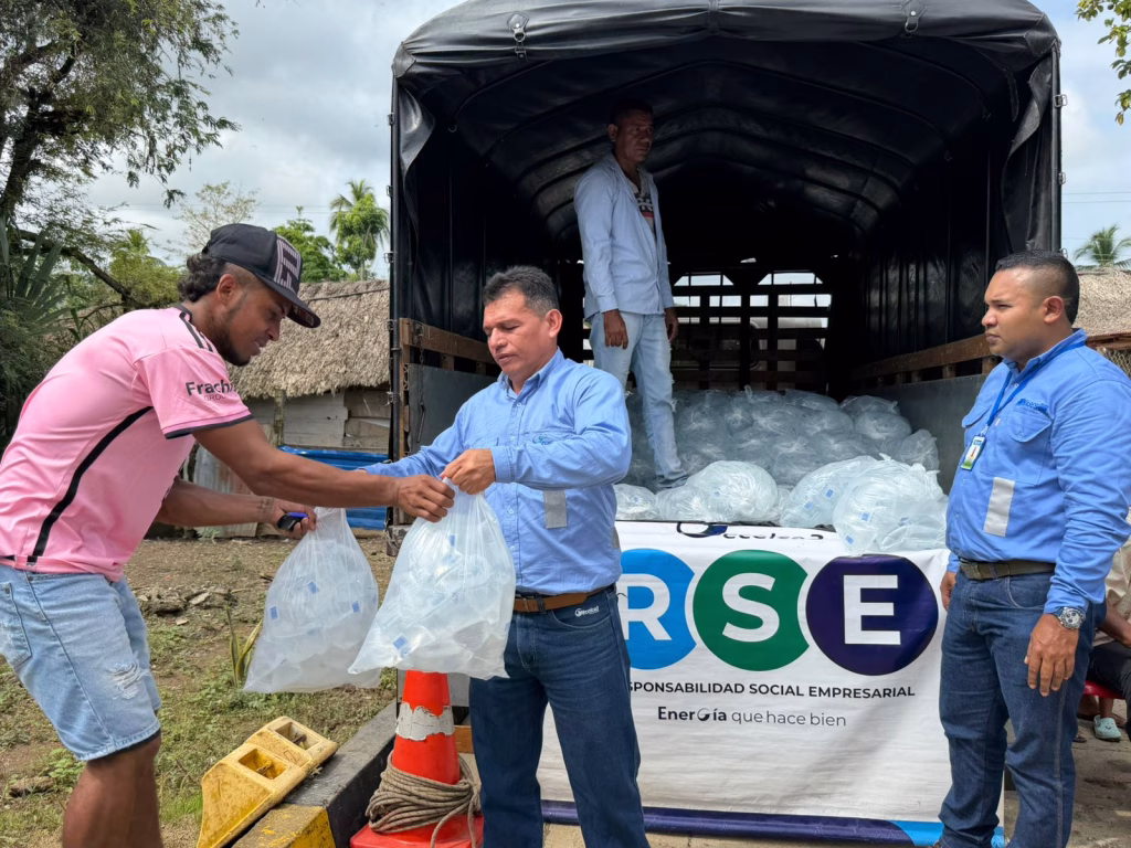 Hombres de la comunidad reciben bolsas con insumos entregados desde un camión durante una jornada de responsabilidad social de GECELCA.