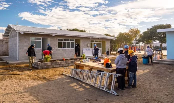 Voluntarios construyen una escuela con bloques de concreto mientras otros trabajan en un huerto comunitario en un entorno rural.