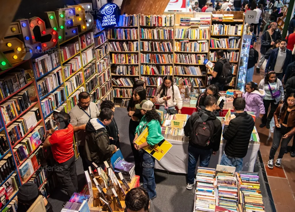 Personas explorando estantes llenos de libros en un espacio cultural con letreros luminosos