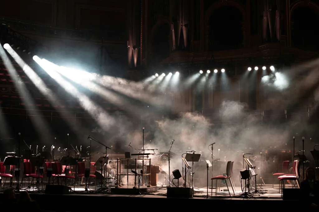 Escenario vacío con sillas, atriles y luces de concierto encendidas antes de una presentación musical