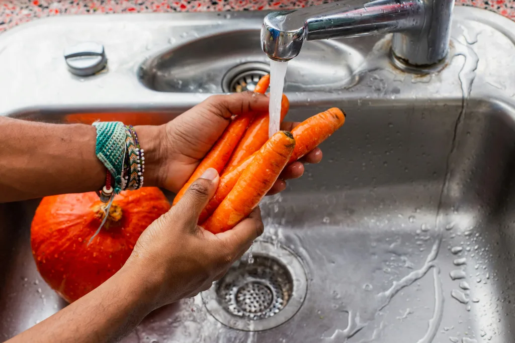 Manos lavando zanahorias frescas bajo el grifo de la cocina