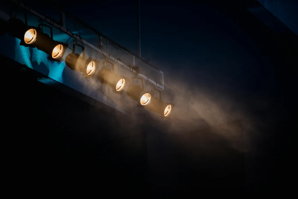 Escenario vacío iluminado con luces púrpura y haces de luz sobre un ambiente teatral oscuro