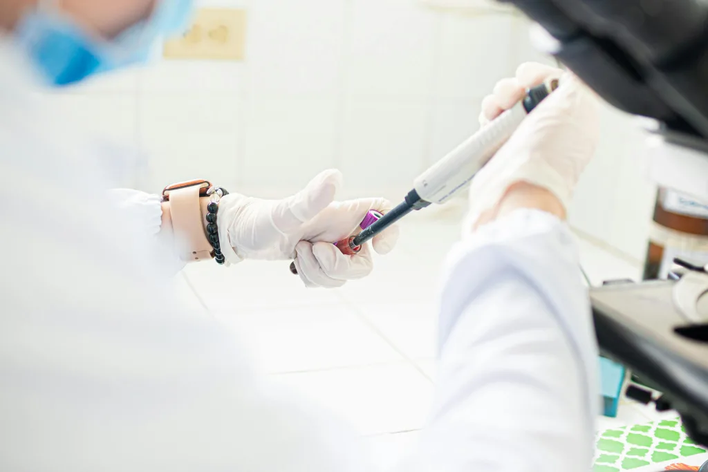 Técnico de laboratorio manipulando muestras con micropipeta en un entorno clínico.