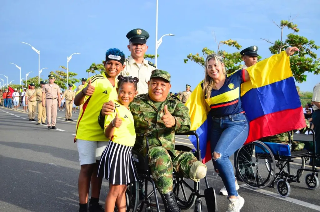 Soldado en silla de ruedas acompañado por ciudadanos y niños durante la celebración del 20 de julio en Barranquilla