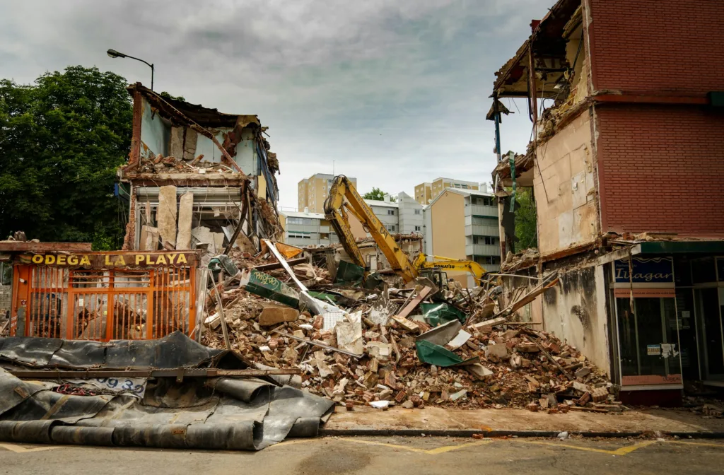 Edificio colapsado con maquinaria removiendo escombros después de un terremoto en zona urbana